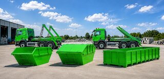 Mehrere grüne Absetz- und Abrollcontainer mit passenden Container-Lkw auf einem sauber organisierten Betriebsgelände. @ 